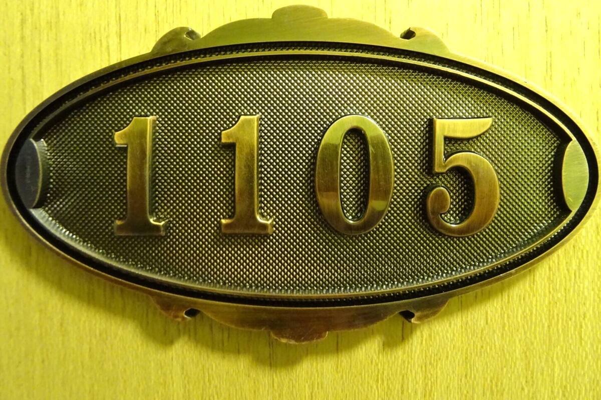 A brass house number plaque with the number 1105 on a yellow wall.