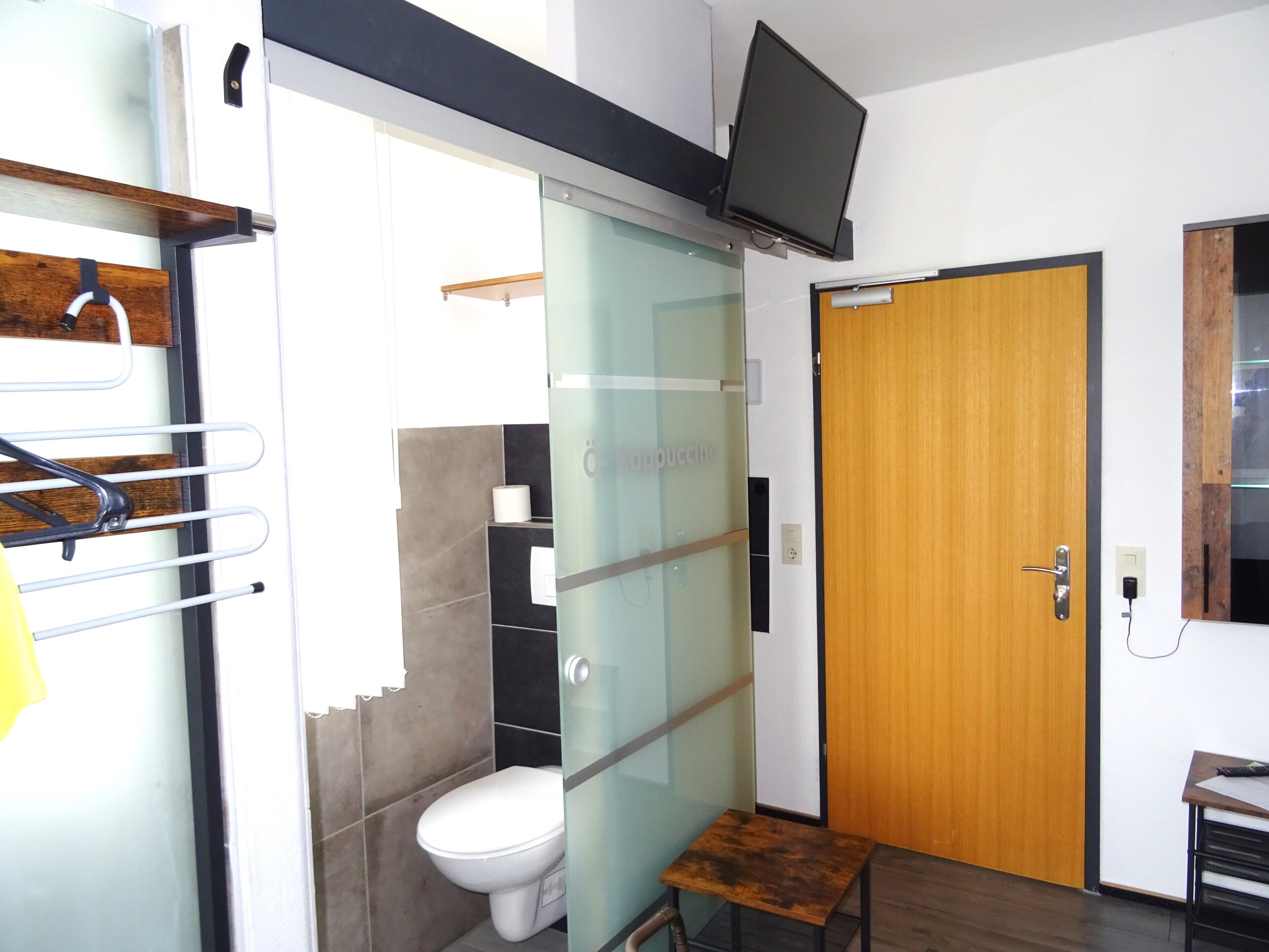 Ein modernes Badezimmer mit Duschkabine aus Glas, Toilette und kleinem Holztisch.