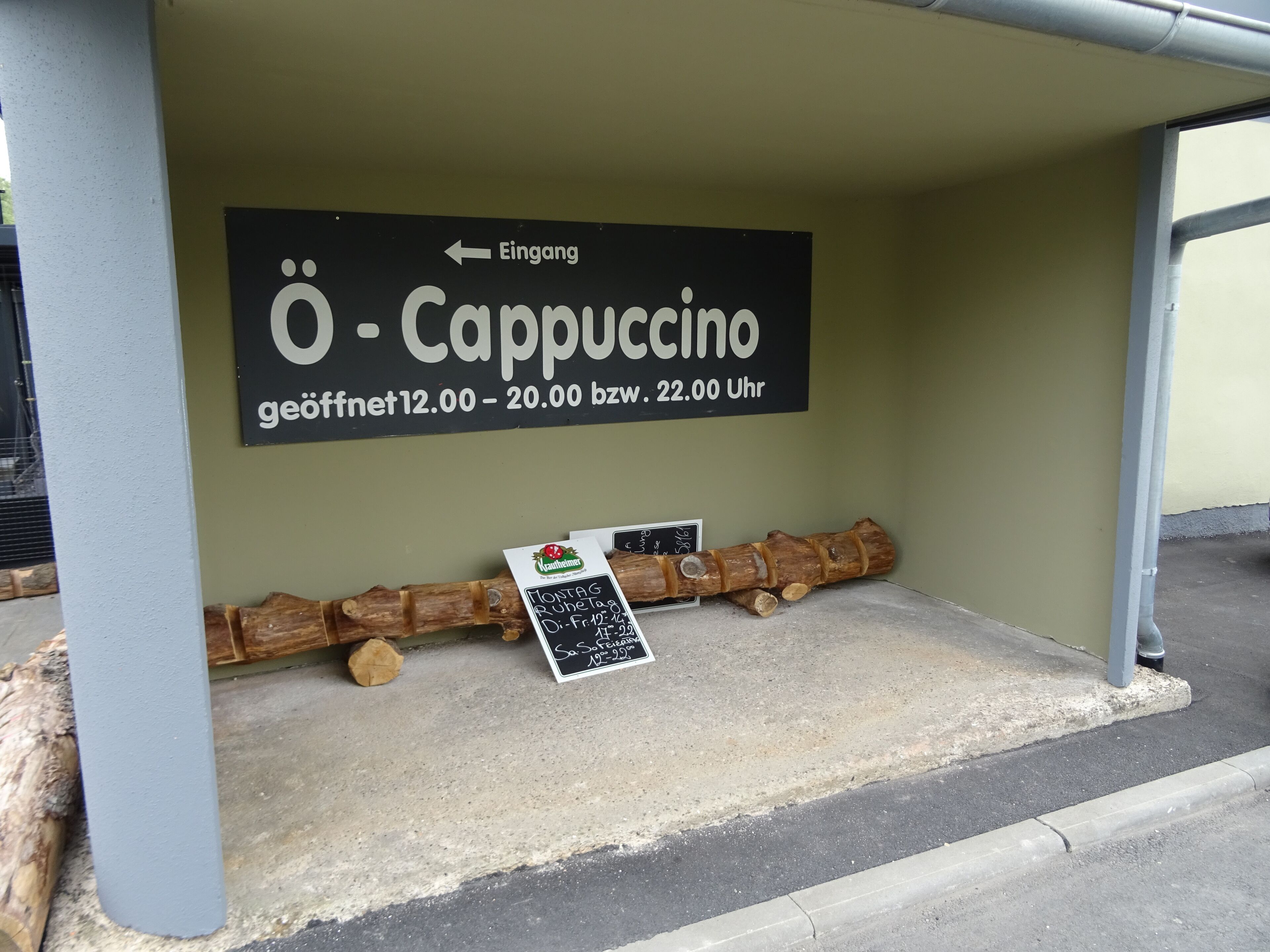 A sign for a coffee shop named "O - Cappuccino" with operating hours and a menu board.
