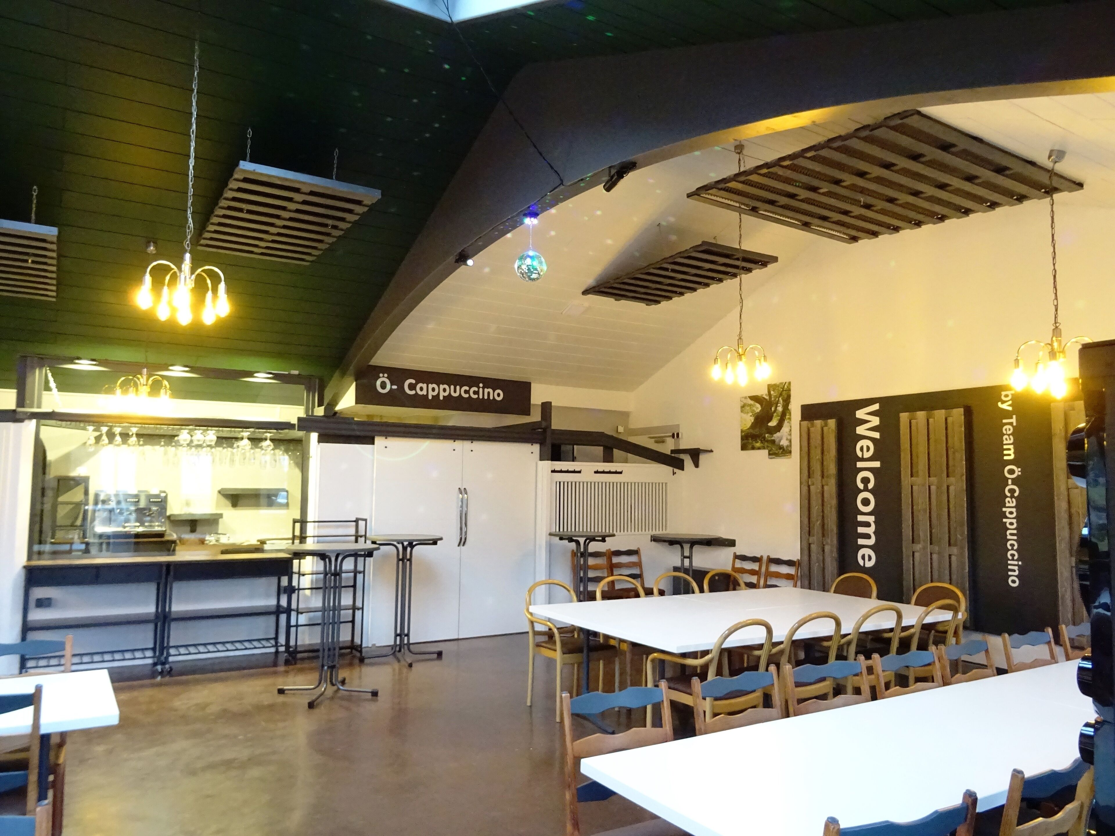 Ein modernes Café-Interieur mit einem langen Gemeinschaftstisch, einzelnen Tischen und hängenden Lampen.
