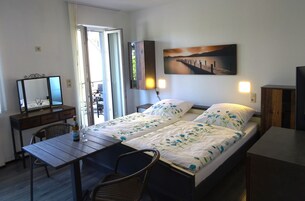 Una cama doble con ropa de cama floral, un escritorio con una silla, un espejo y un cuadro de un muelle en la pared.