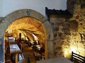 Un espacio comedor subterráneo con paredes de piedra, mesas de madera y sillas de metal.