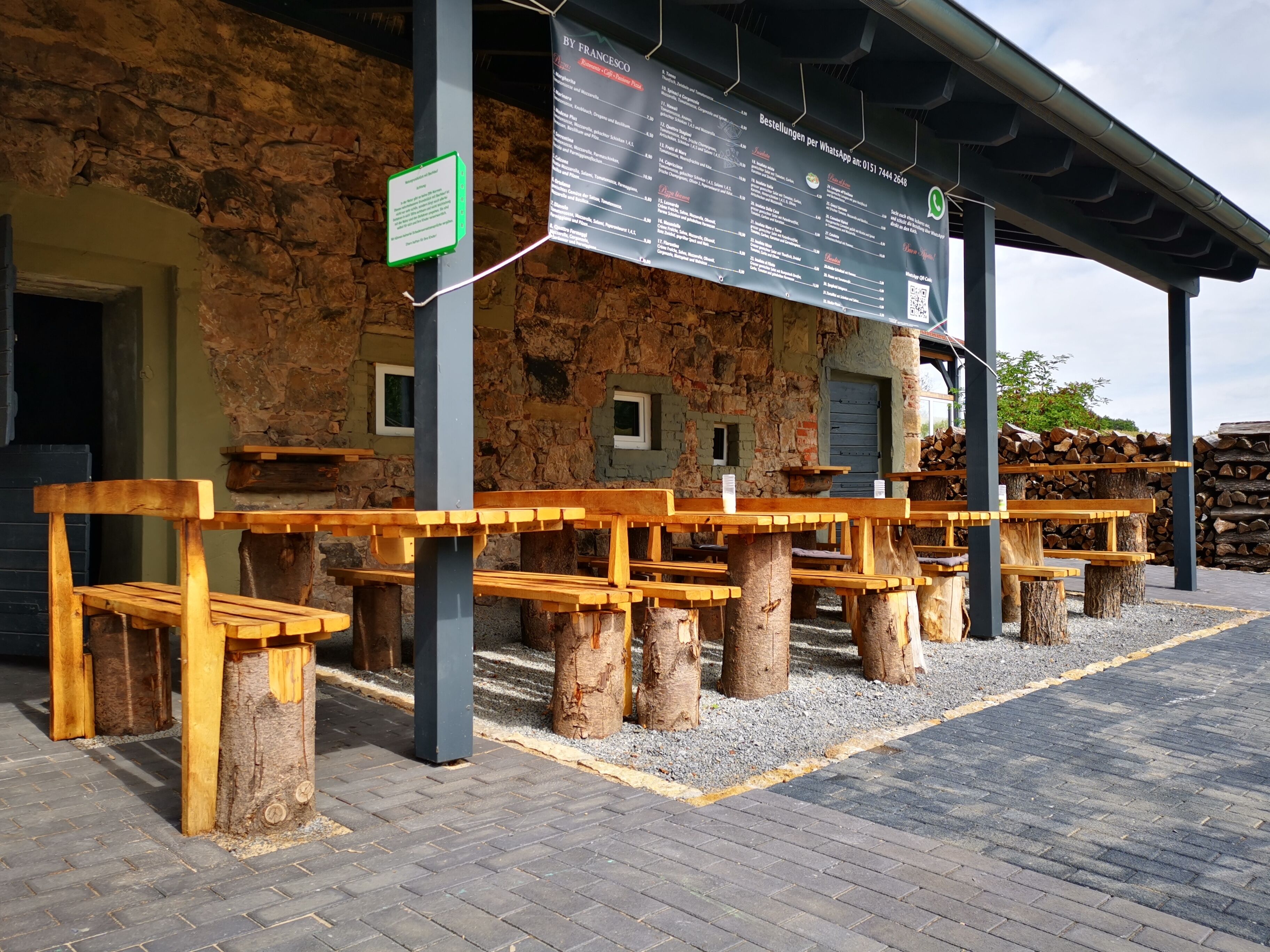 Holzbänke im Freien mit Tischen, ein Steinhaus und eine Speisekarte.