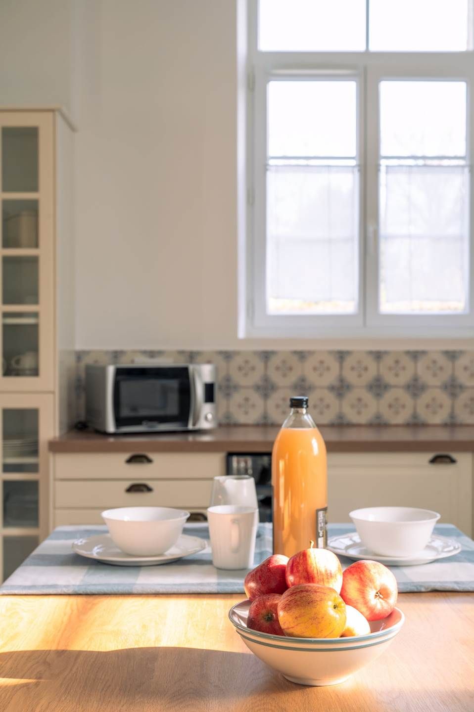 Een keuken met een magnetron, een fles sinaasappelsap en een schaal appels op het aanrecht.