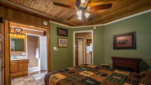 Un dormitorio con techo de madera, una cama grande con colcha, un espejo y una chimenea.