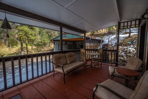 A covered porch with a wooden bench, a table, and chairs. A building with a green roof is visible in the background.