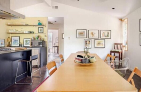 Un espace repas avec une longue table en bois, des chaises et une cuisine en arrière-plan.