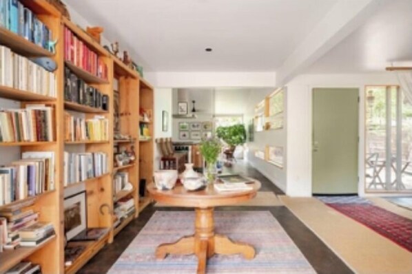 Un couloir avec des étagères à livres, une table ronde en bois surmontée d’un vase et un tapis rouge.
