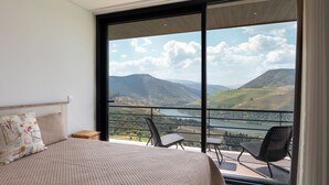 A bedroom with a large bed, a nightstand, and a view of a lake and mountains through a sliding glass door. - Feel Discovery Alvim's Douro (Armamar)