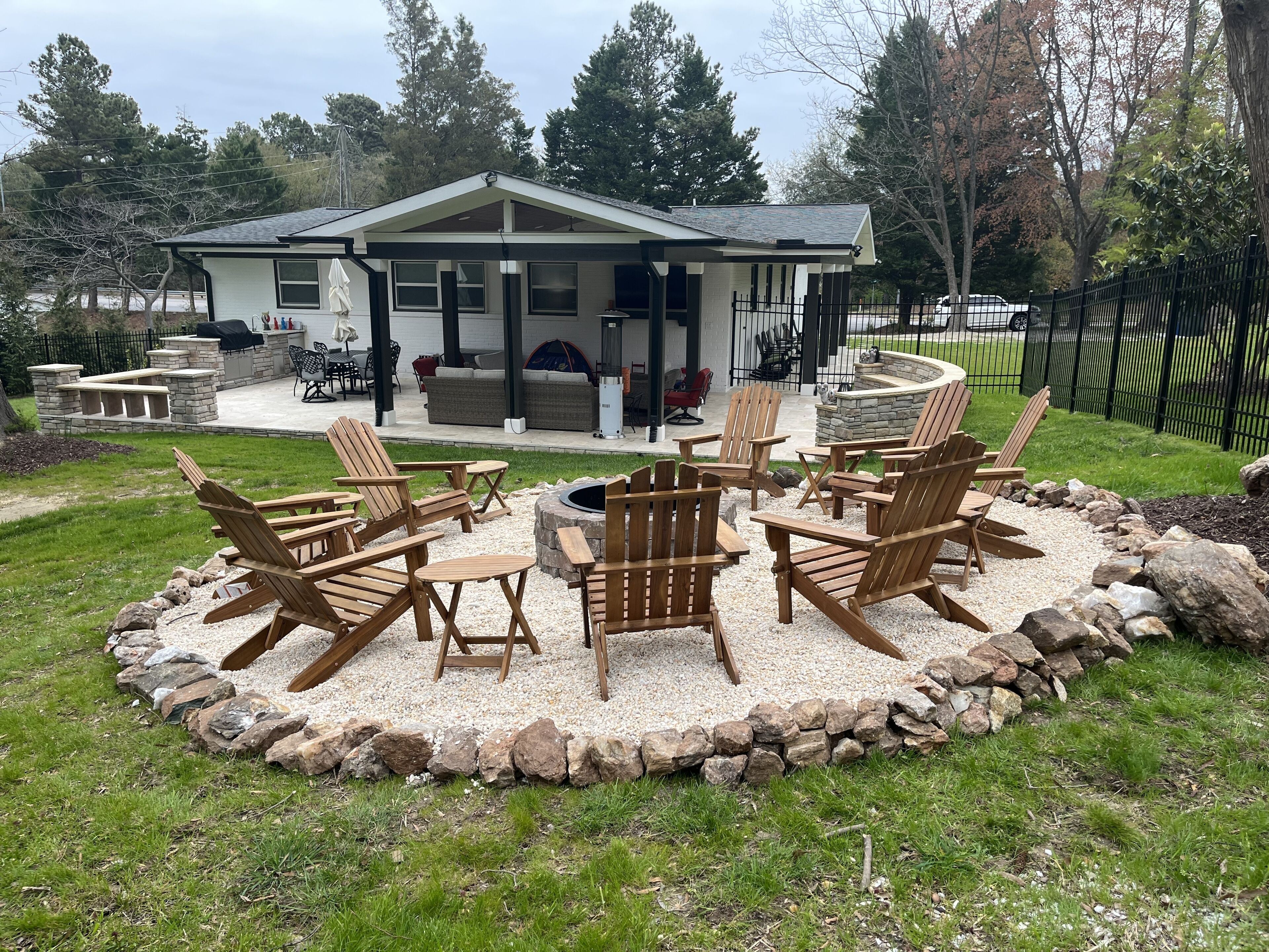 Una casa con un patio che include poltrone Adirondack, un braciere in pietra e un muro in pietra attorno alla zona salotto.