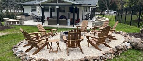 Una casa con un patio che include poltrone Adirondack, un braciere in pietra e un muro in pietra attorno alla zona salotto.