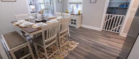 Comedor con una mesa de madera dispuesta para cuatro personas, rodeado de sillas blancas.