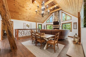 A wooden interior with a dining area, a stone fireplace, and large windows. - 'Make Your Mark' Cozy Sapphire Cabin with Hot Tub (Sapphire)