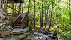 Una terraza de madera con una escalera que lleva a un espacio cubierto, rodeada de bosque.