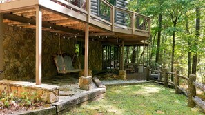 A rustic cabin with a stone exterior, a wooden deck, and a swing chair. - 'Make Your Mark' Cozy Sapphire Cabin with Hot Tub (Sapphire)