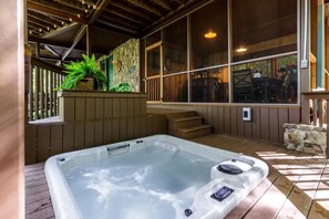 Un bain à remous doté d’un mur en pierre et d’une terrasse en bois, entouré de fenêtres et agrémenté d’un escalier.