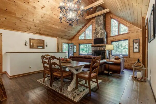 Un intérieur de chalet chaleureux avec un coin repas, une cheminée et de grandes fenêtres.