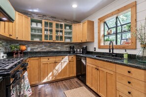 A kitchen with wooden cabinets, a granite countertop, and a window with a view of greenery. - 'Make Your Mark' Cozy Sapphire Cabin with Hot Tub (Sapphire)