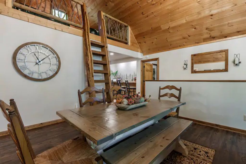 A dining area with a wooden table, benches, and a clock on the wall.