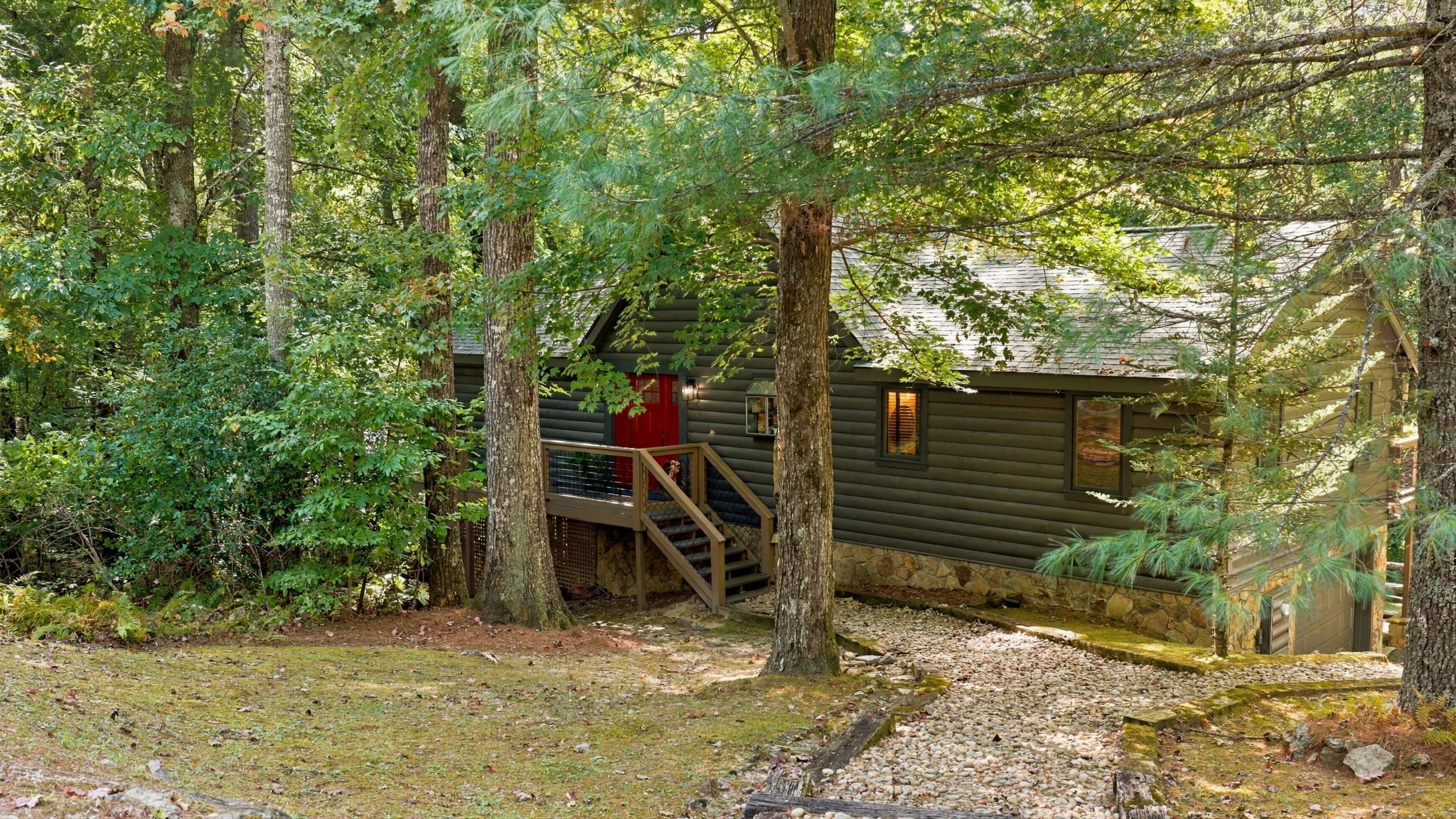 Une cabane avec un escalier en bois menant à une porte rouge, le tout entouré d’une forêt dense.