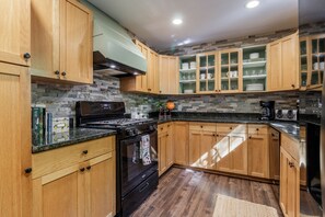 A kitchen with wooden cabinets, a black stove, and a stone backsplash. - 'Make Your Mark' Cozy Sapphire Cabin with Hot Tub (Sapphire)