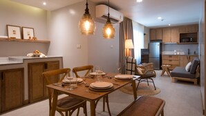 A modern kitchen with wooden cabinets, a dining area with a table set for four, and a living area with a sofa and a lamp. - EXECUTIVE SUITE (จ.เชียงใหม่)