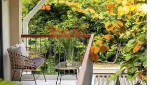 Un balcon agrémenté d’un fauteuil en osier et d’une petite table, entouré d’une végétation luxuriante et offrant une vue sur un jardin.