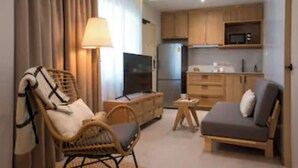 Un espacio habitable compacto con sofá, sillón, mesita, televisor y kitchenette con armarios y microondas.