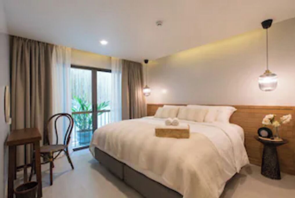 A hotel room with a large bed, a small table, a chair, and a view of the outdoors through a window.