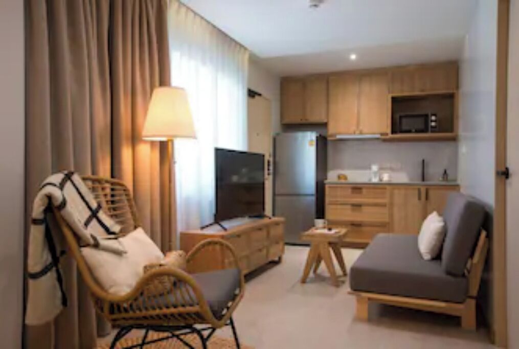 A compact living space with a sofa, a chair, a small table, a TV, and a kitchenette with cabinets and a microwave.