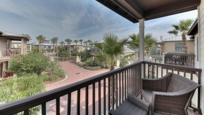 A balcony with wicker furniture, a paved walkway, and a view of a residential area with palm trees and houses. - On 30A, 4 Houses from Beach with Beachfront Pool, between Rosemary and Alys (Seacrest Beach)