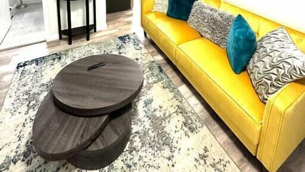 A modern living room with a yellow sofa, a round coffee table, and a patterned rug. - Newly 5 Star Rental (New York)