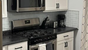 A kitchen with white cabinets, a stainless steel microwave, a gas stove, and a toaster. - Newly 5 Star Rental (New York)
