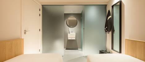 Una habitación de hotel moderna con dos camas, un espejo grande y un baño visible a través de una puerta abierta.
