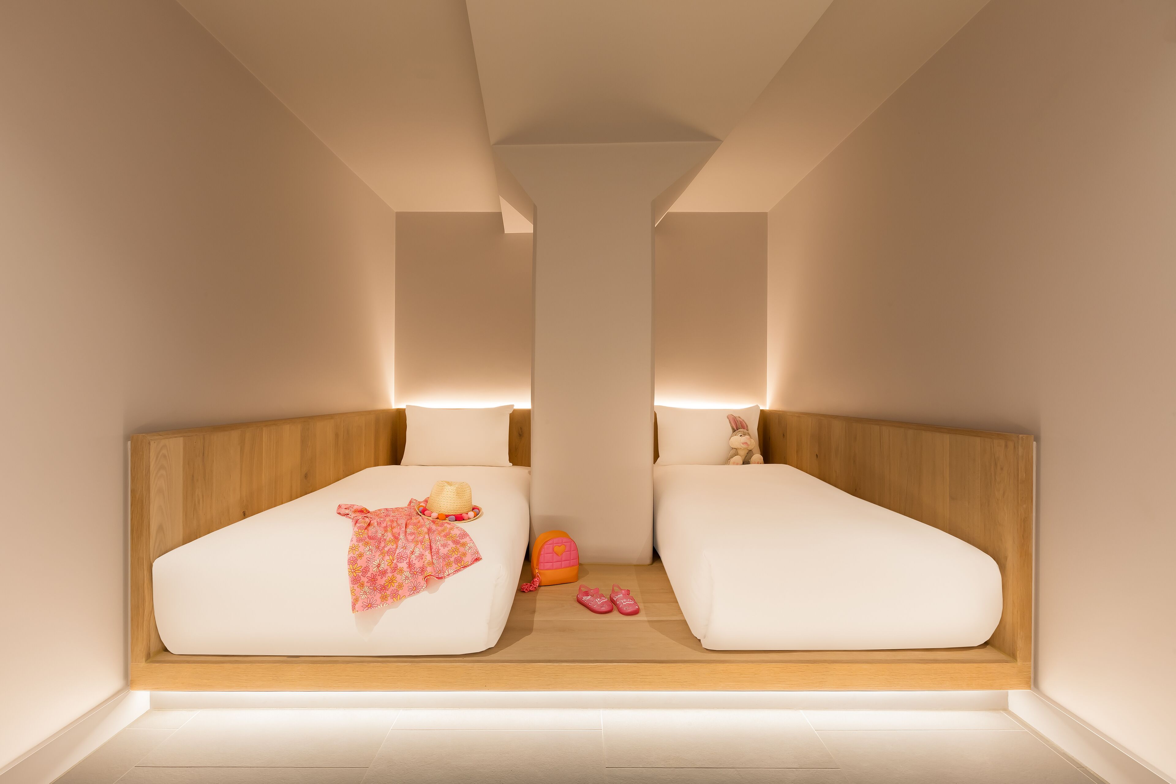 A modern, minimalist room with two beds, a small table, and a wall-mounted shelf.