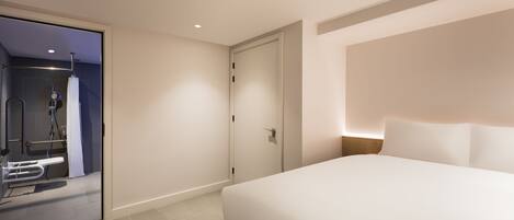 Una habitación de hotel moderna con una cama grande, un vestidor amplio y un baño separado con ducha e inodoro.