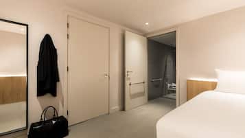 A hotel room with a large bed, a wardrobe, a bathroom with a shower, and a hanging robe.