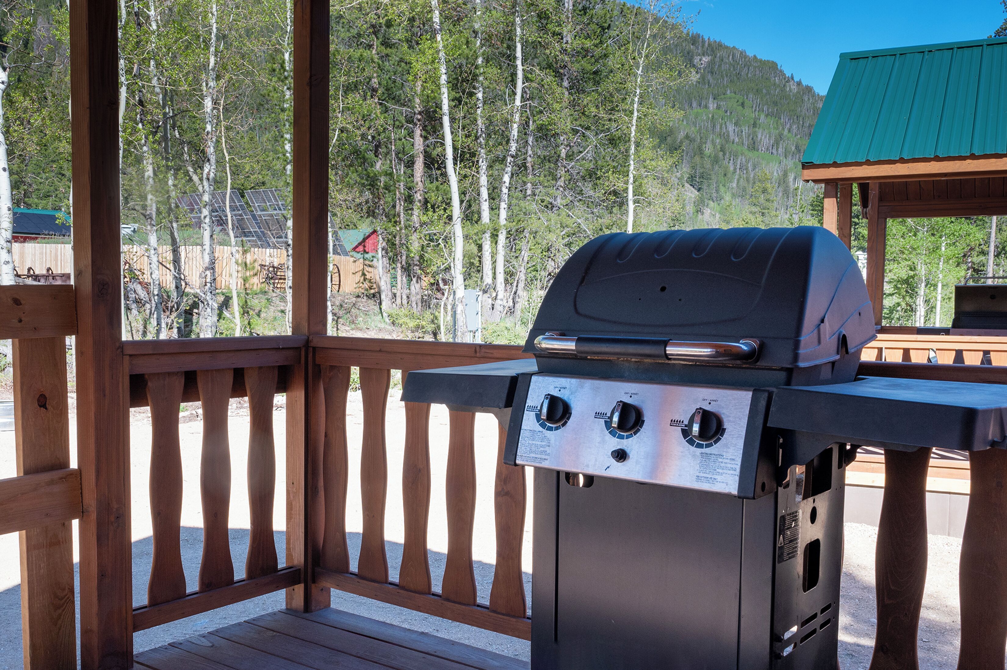 A barbecue grill on a wooden deck with a view of a forested mountain in the background.