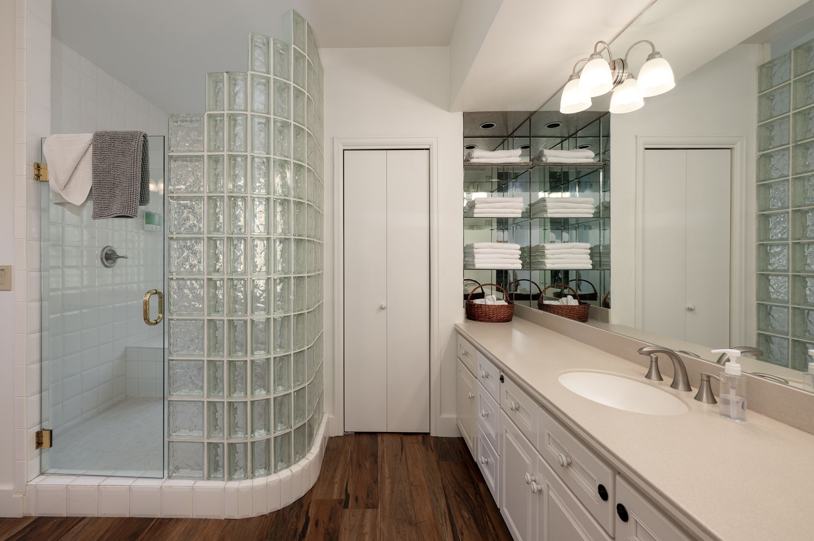 A modern bathroom with a glass shower enclosure, a large vanity with a sink, and a mirrored wall.