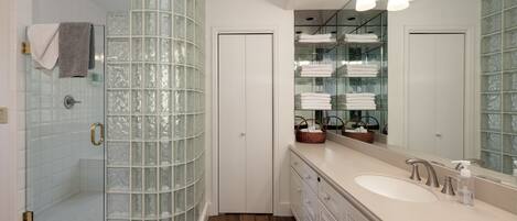 A modern bathroom with a glass shower enclosure, a large vanity with a sink, and a mirrored wall.