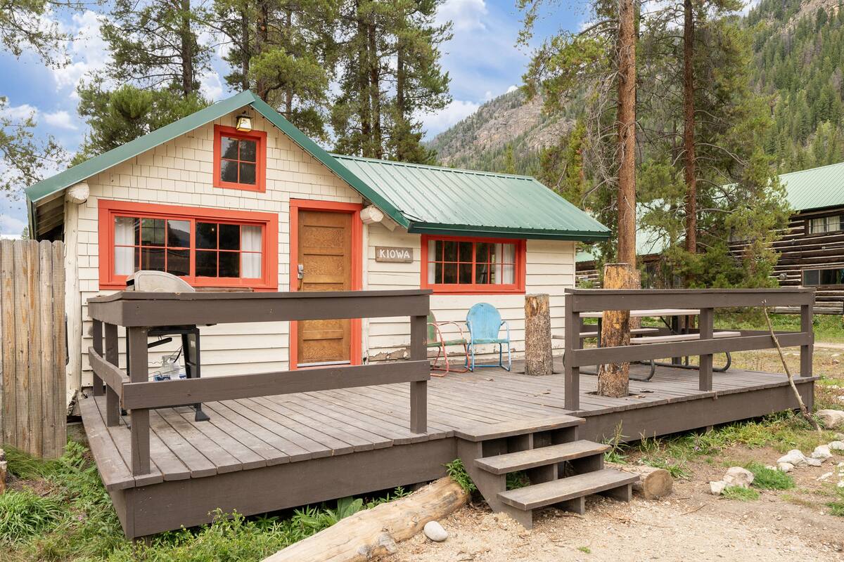 A cabin with a green roof, red trim, and a wooden deck with benches.