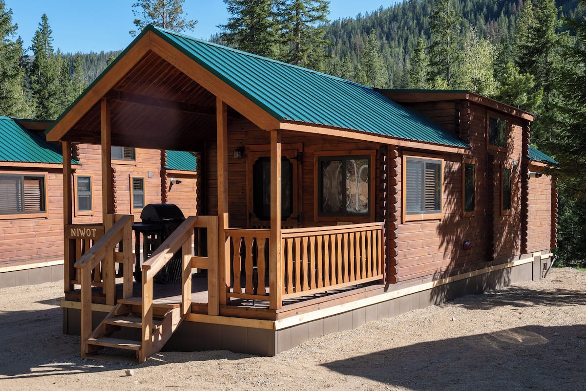 A log cabin with a porch, a grill, and a view of a forested mountain.