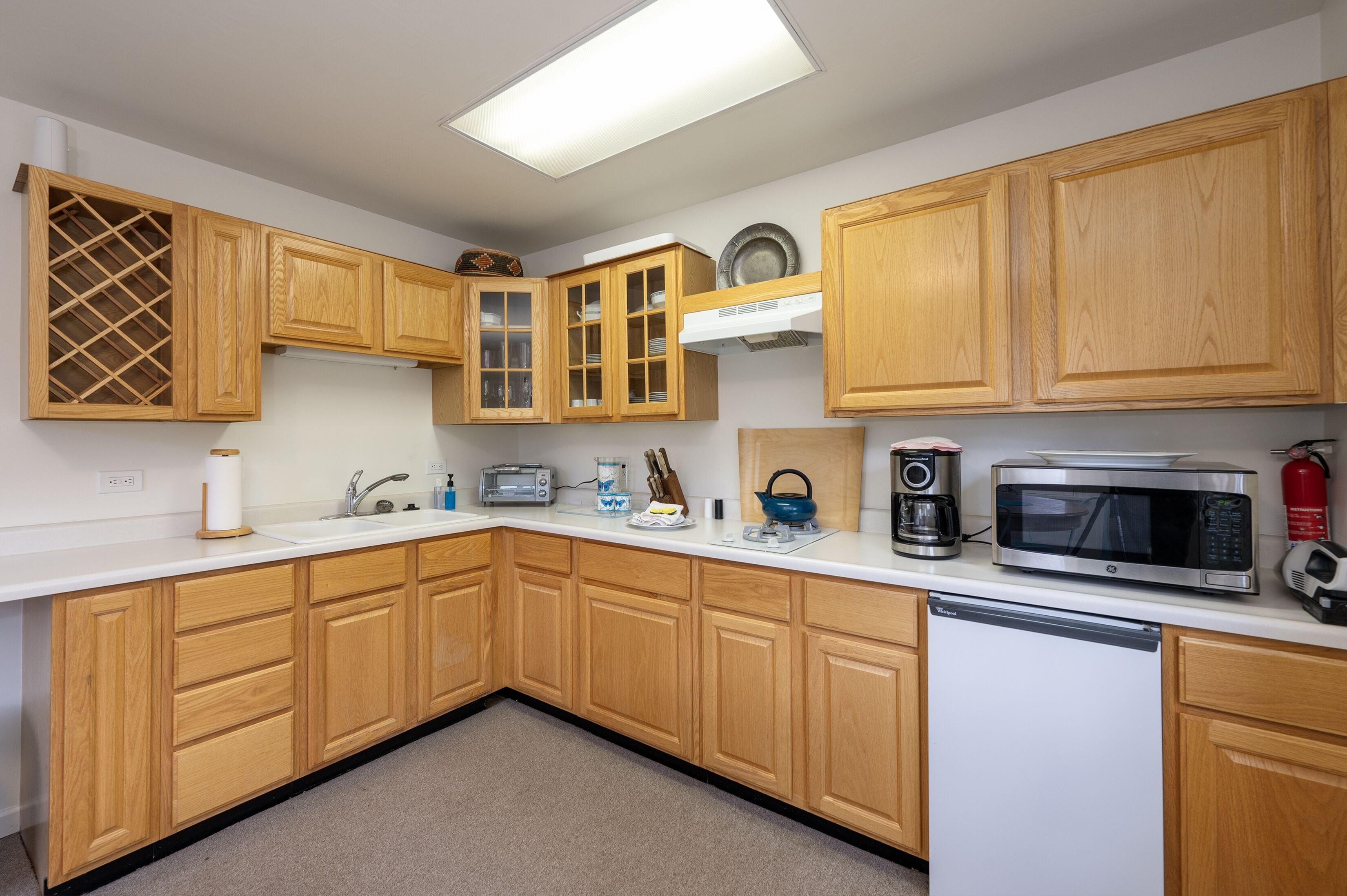 A kitchen with wooden cabinets, a white countertop, a dishwasher, a microwave, a toaster, a kettle, and a coffee maker.
