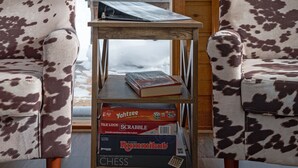 Et værelse med to stole i lædermønster, et træbord med brætspil og udsigt til snedækkede bjerge gennem store vinduer.