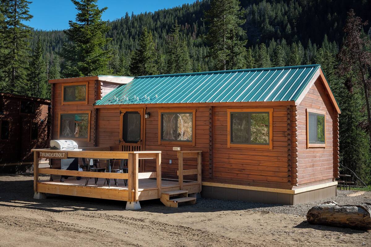 A wooden cabin with a metal roof, a deck, and a grill area.