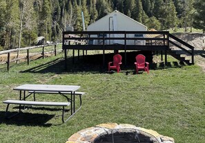 A rustic cabin with a deck, a picnic table, and two red chairs.