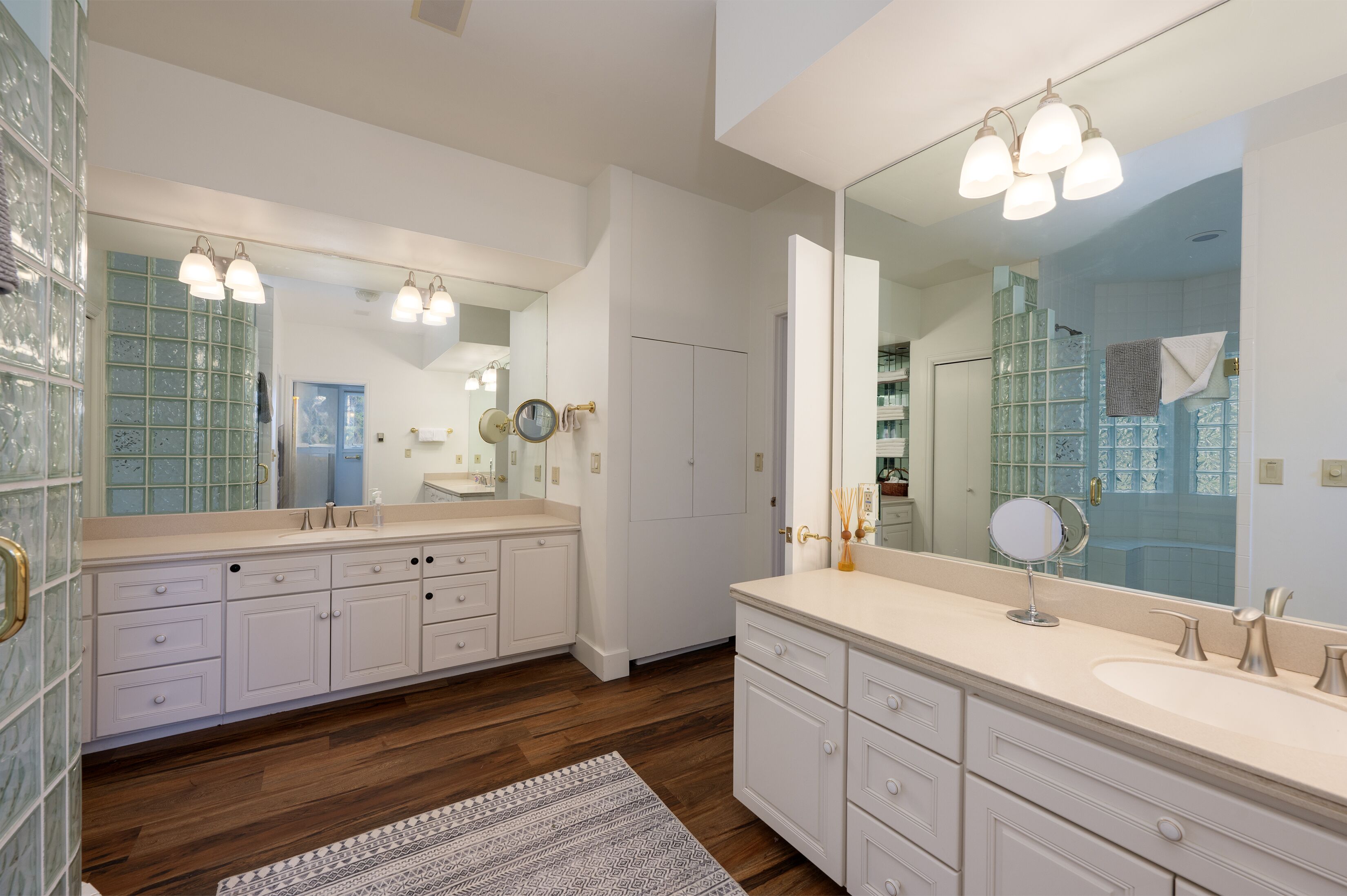 A modern bathroom with a large mirror, two sinks, and a walk-in shower.