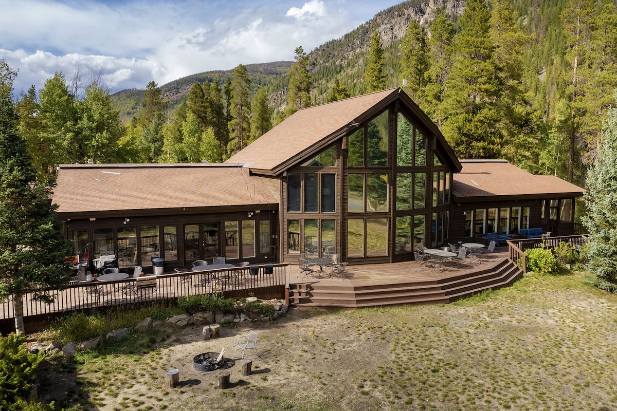 A lodge with a large deck, outdoor seating, and a scenic mountain backdrop.