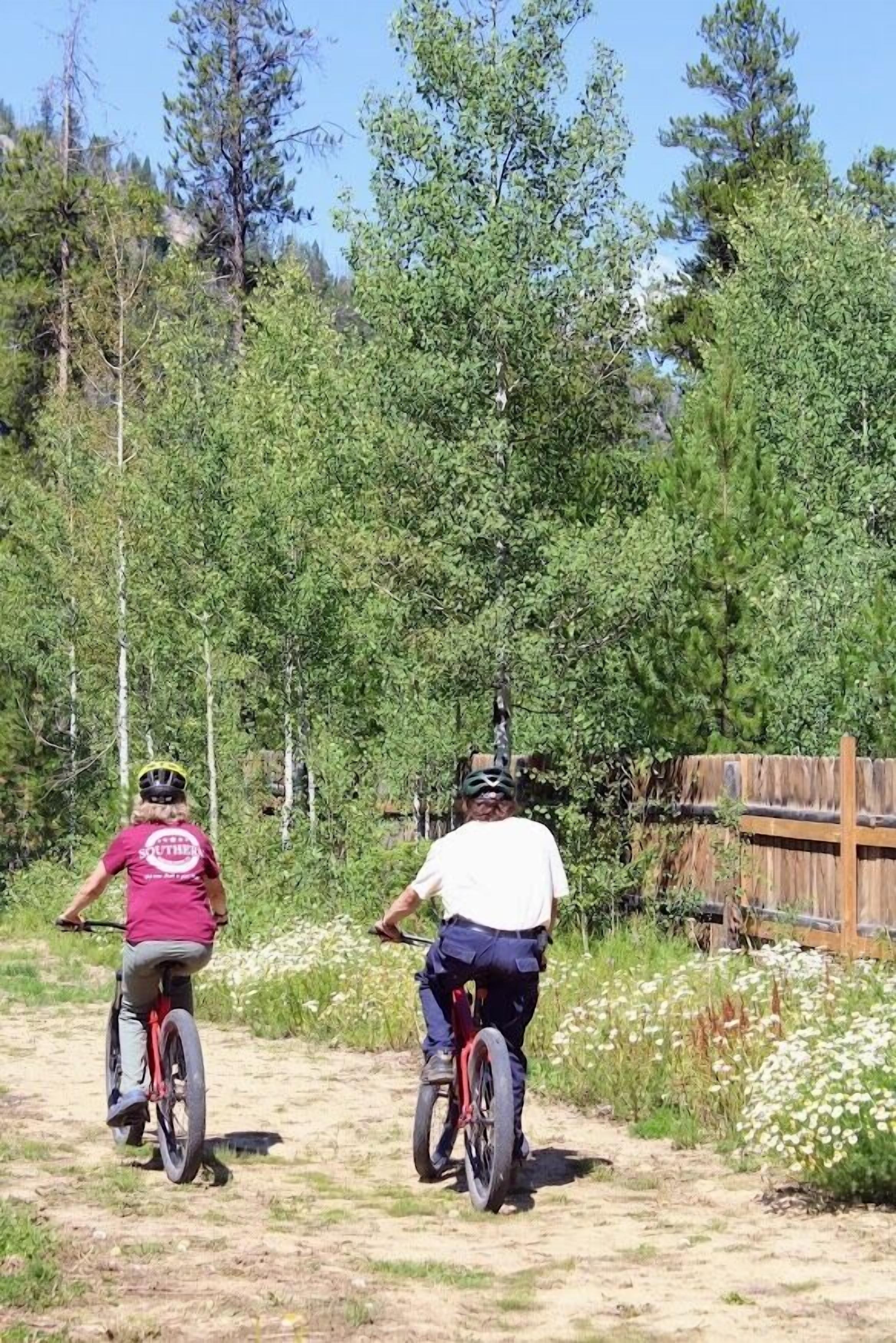 Twee personen fietsen op een onverhard pad, omringd door begroeiing en een houten hek.