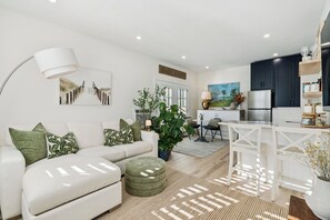 Un salon moderne avec un canapé blanc, des coussins verts, une table basse et un coin repas comprenant une table et des chaises blanches.